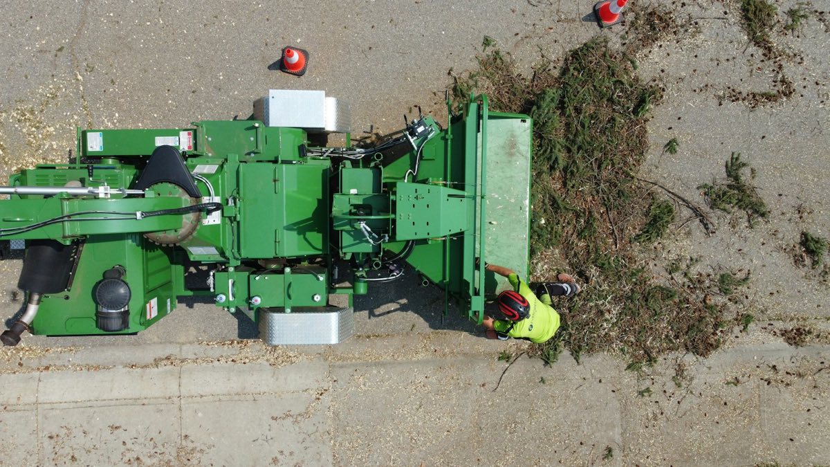 Aerial view of a worker in a helmet feeding cut branches into a wood chipper