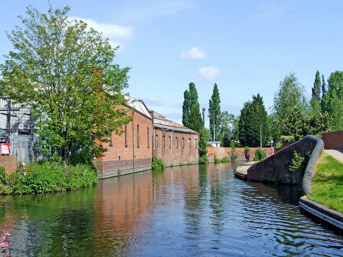 The Staffordshire and Worcestershire Canal passing old brick mill buildings and trees in Kidderminster
